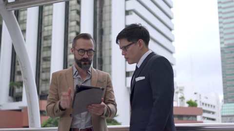 Two Business people Caucasian with Asian man colleague partnership discussing business project plan with using digital tablet in the city. Business meeting, technology, mergers and acquisition concept