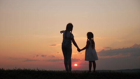 happy family two sisters walks at sunset in the park silhouette. two daughters hold hands outdoors. kid dream concept. happy family walk together. children little kid sunset walking in the park