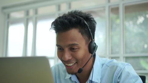 close up call center latin man wear a headset to talking with a customer and working at computer desktop in operation room for helpline and telesales service desk support concept.