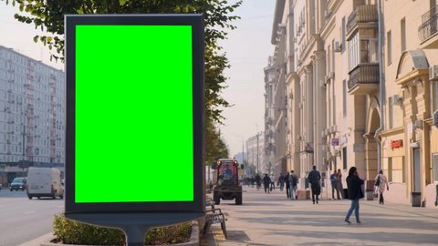 Green screen billboard located on a busy street. Cars move in a stream. Working day morning. People walk along the sidewalk. Cleaning equipment is working