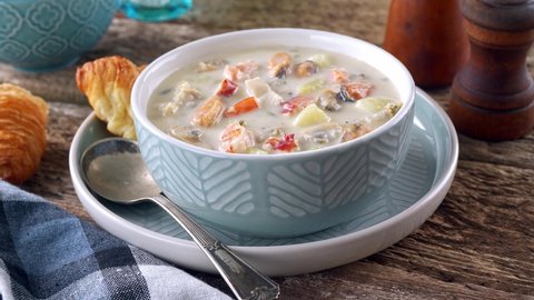 A bowl of delicious seafood chowder with fresh clams, mussels, lobster, shrimp, scallops, potato, celery and cream.
