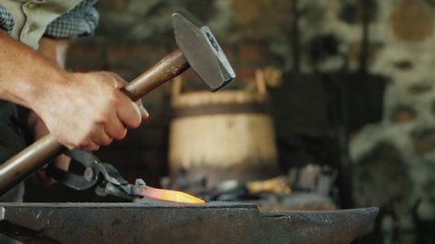 A blacksmith with forceps holds a red-hot billet above the anvil, striking it with a hammer. Traditional crafts