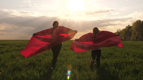Children in red raincoats play superheroes running in a green meadow. Children's games and dreams. Slow motion. teenager dreams of becoming a superhero. young girls in a red cloak.
