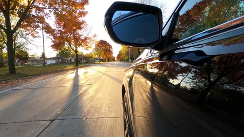 Driving a black SUV car down a suburban street in fall season. Colorful trees, red orange yellow foliage, sunset sun shining. The Autumn colors 