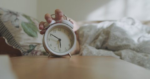 
Get up early in the morning on the clock. Sleeping man reluctantly wakes up to an alarm clock early in the morning. The man's hand stops the alarm clock to sleep longer.
