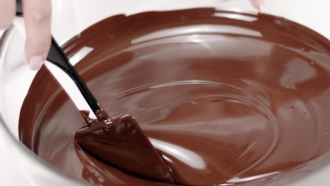 silicone spatula stirs dark melted chocolate in glass bowl slow mo close up. Preparation of High quality melted chocolate without lumps for premium handmade candies, truffles, chocolates and sweets.