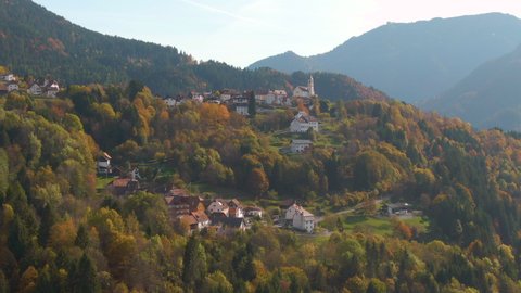 AERIAL Beautiful flying view of idyllic mountain village on a scenic fall day. Flying around a small town in the Dolomites surrounded by forest changing colors in autumn. Drone shot of Italian country
