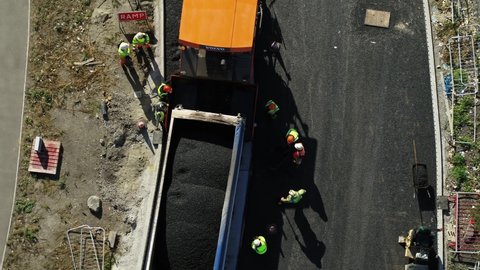 Top down aerial view of a tipper lorry connecting to a tarmac machine ready to resurface a new road.