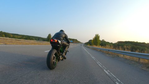 Biker is driving motorbike during road trip at autumn sunset time. Man ride fast on modern sport motorcycle at highway. Motorcyclist racing his bike on country road. Concept of adventure. Aerial shot