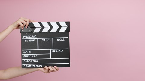 Close up female hold making movie production clapperboard on pink background.