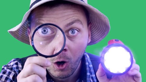 A funny private detective with a flashlight looks at the camera through a magnifying glass looking for valuable information. Chromakey