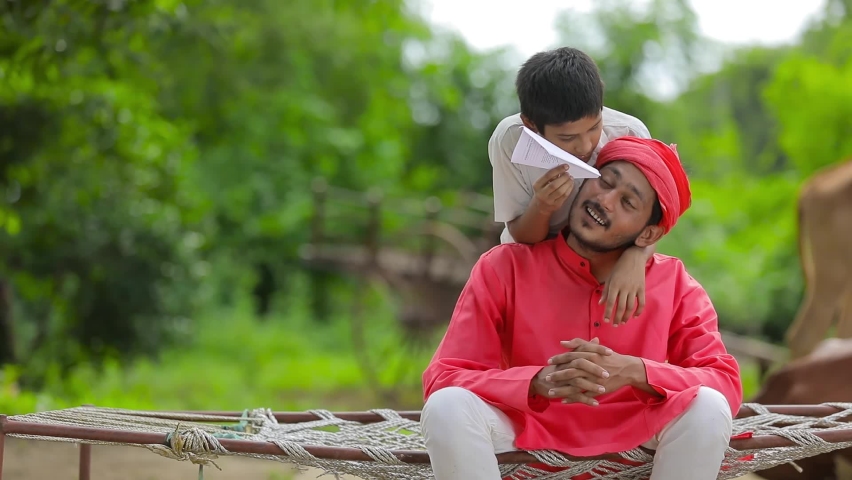 young indian farmer with his child playing with handmade paper airplane 