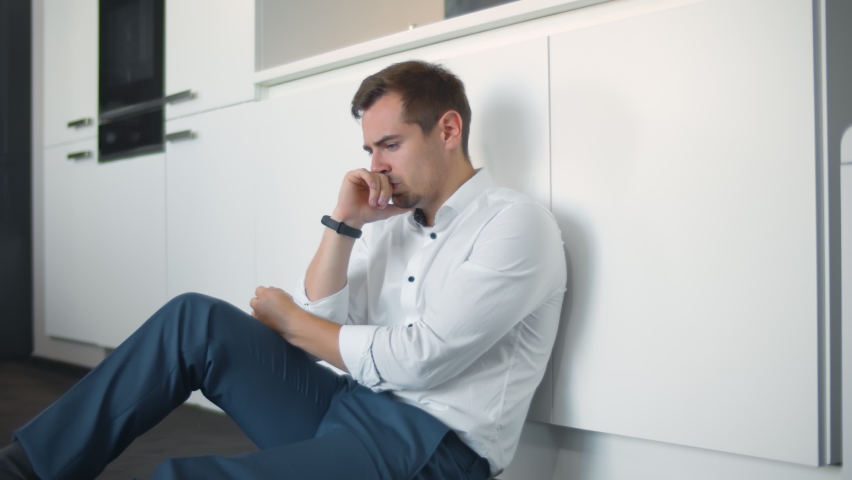 Depressed young businessman sitting on floor in kitchen. Portrait of anxious handsome man on kitchen floor having business or personal problems feeling stressed and desperate Royalty-Free Stock Footage #1060591657