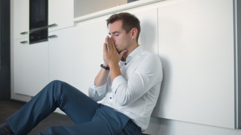 Depressed young businessman sitting on floor in kitchen. Portrait of anxious handsome man on kitchen floor having business or personal problems feeling stressed and desperate