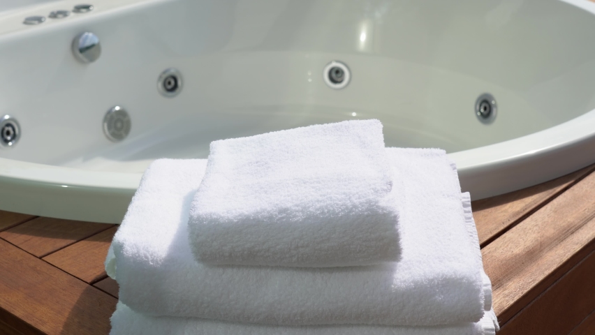 Woman puts one clean soft white towel on stack of folded several towels near empty whirlpool bath. | Shutterstock HD Video #1060592716