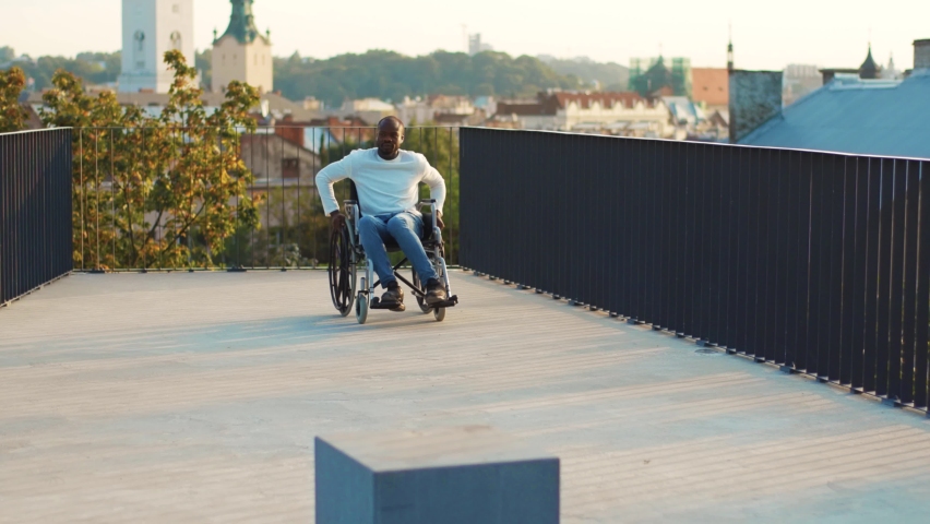 Close up young man listening music on headphones on a wheelchair in a park look around at sunlight outdoors. Disability cell call handicap injured sitting health care. Slow motion