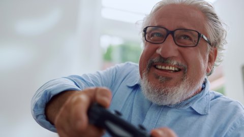 Portrait of smiling senior man playing video game. Emotional old man using gamepad for computer game. Happy man holding joystick. Closeup male person with grey hair making grimaces during video game