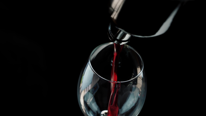 Wine. Pouring red wine into glass from the bottle on the black background. The camera moves around the bottle and glass of wine. Slow-motion shot in close-up Royalty-Free Stock Footage #1060599733
