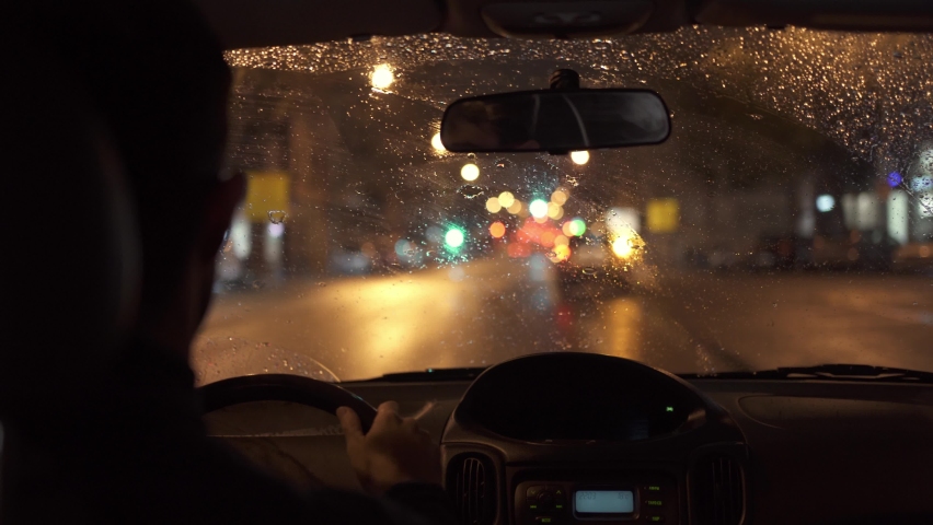 Car driving through a heavy storm in a dark rainy city. Night lights and rain seen through the interior of a vehicle while a man drives. Royalty-Free Stock Footage #1060600090