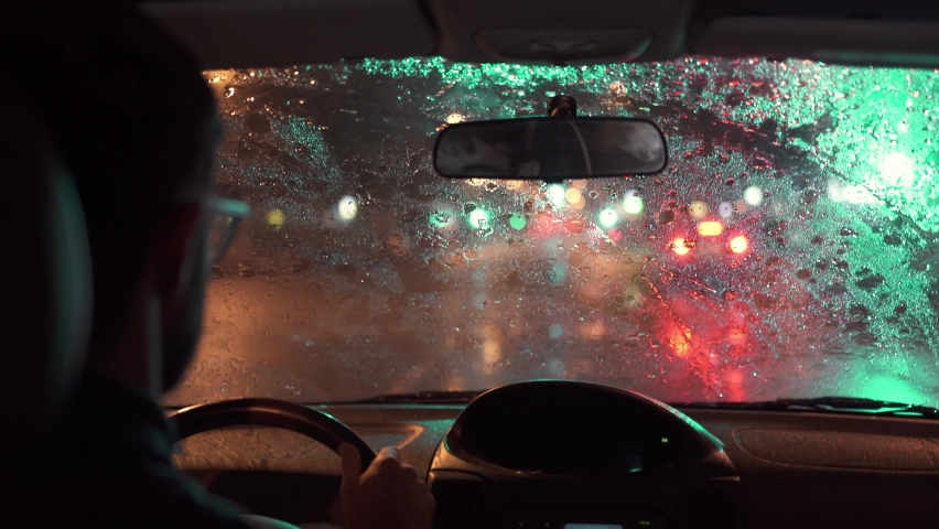 Car driving through a heavy storm in a dark rainy city. Night lights and rain seen through the interior of a vehicle while a man drives.