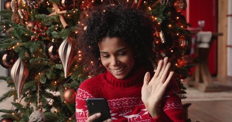 African woman holds smart phone make video call on Christmas Eve congratulates relatives 2021 enjoy remote talk dances feels cheery celebrates New Year, videocall and modern comfort tech usage concept