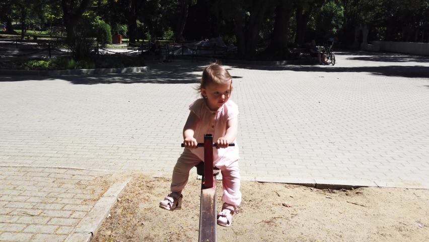 Little girl having fun on outdoor playground. Swinging on see-saw. 