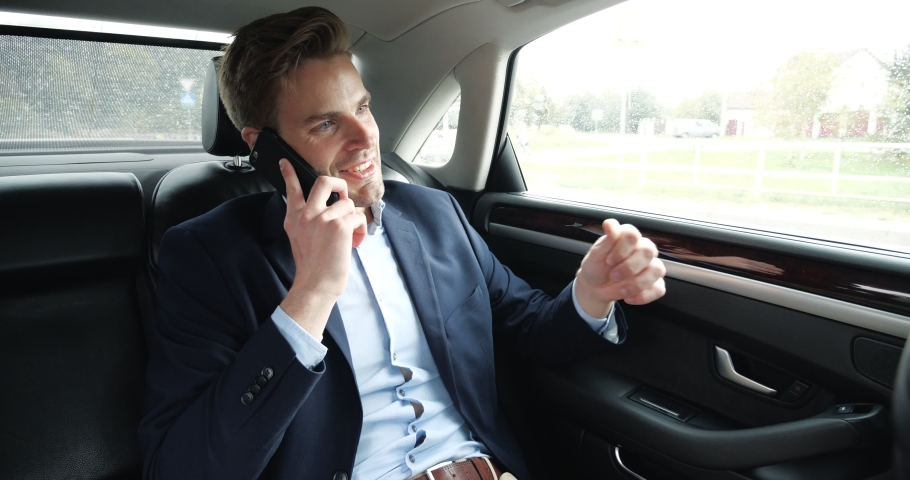 A Confident Businessman is talking on his Phone while traveling in Business Class Car. A handsome Caucasian Male in his Elegant Expensive Car while riding with his own Driver. Successful Lifestyle. Royalty-Free Stock Footage #1060603066