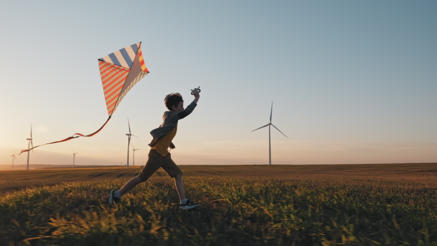 Happy boy runs launches bright kite into sky mown wheat field, playing with wind in field of an orange sunset on day lens flares wind turbines in summer slow motion. School break. Lifestyle. Childhood Royalty-Free Stock Footage #1060603840