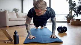 Portrait of man with tablet doing push-ups workout exercise indoors at home.