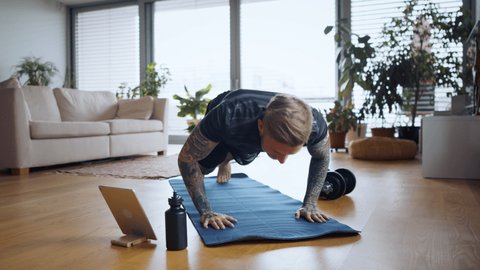 Portrait of man with tablet doing push-ups workout exercise indoors at home. 库存视频