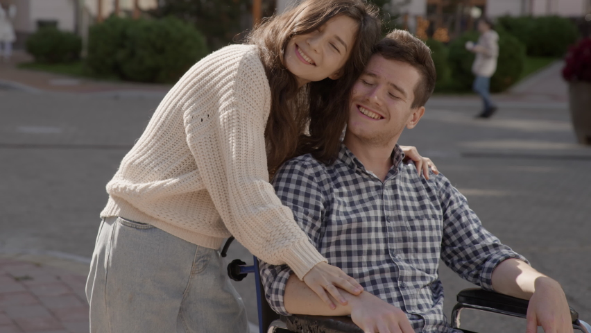 Portrait of disabled happy young man n wheelchair and his wife or friend looking at camera. Caucasian handicapped guy with paralysis living full life. Couple in love. 6k downscale 10 bit color.