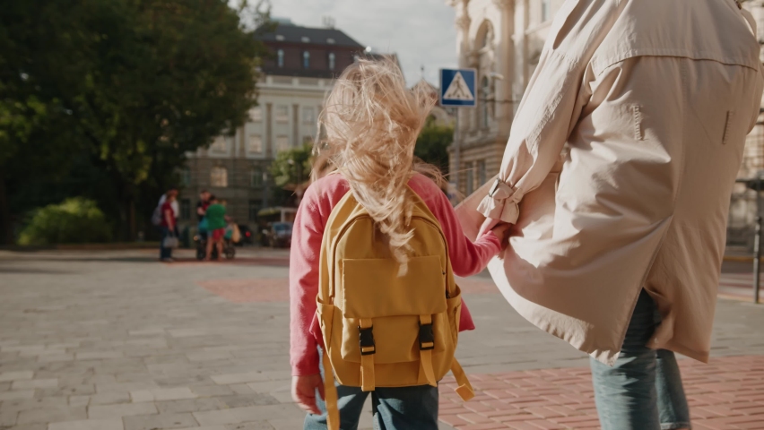 Shot back woman holding hand of little schoolgirl walking smiling going to school outdoors on street. Child smiling feel happy. Study outdoors backpack. Slow motion Royalty-Free Stock Footage #1060605010