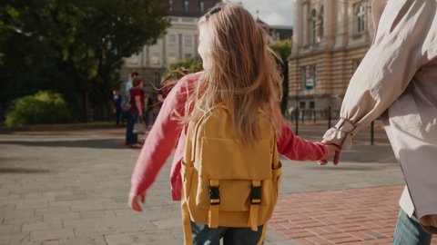 Shot back woman holding hand of little schoolgirl walking smiling going to school outdoors on street. Child smiling feel happy. Study outdoors backpack. Slow motion