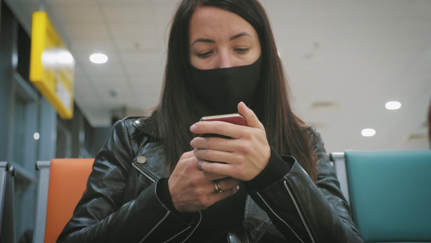 A young beautiful girl sits in the airport waiting room and uses a mobile phone. Woman buying e-ticket, making hotel reservations and checking in online.
