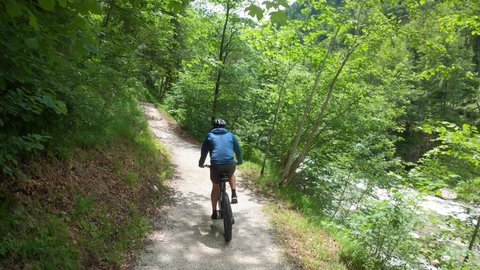Mountain Biker riding on a narrow trail through a lush forest, Austrian Alps