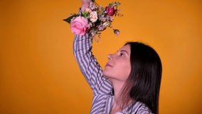 A young girl in natural make up rotating a bunch of flowers above her head, enjoying the romantic bouquet and smiling to camera. 4K Footage, isolated on yellow background