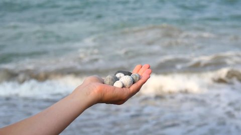 Beautiful round gray and white sea stones lie in a female hand against background of sea and waves. The concept of relaxation, vacation and meditation, zen, Cyprus. Slow motion video.