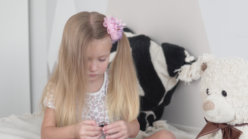 A cute little girl combs her hair with a comb. The child braids his hair in a ponytail