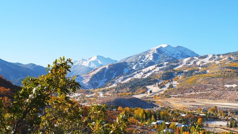 High angle aerial panning view of Aspen city, Colorado by Rocky mountains of winter snow covered highlands and small airport runway in roaring fork valley in autumn