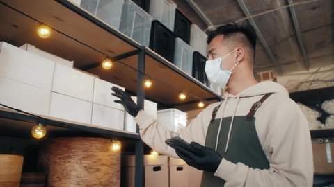 Asian korean man worker wearing protective face mask and check stock in warehouse. Concept new normal work in industry, factory after coronavirus Covid 19 pandemic, e-commerce goods delivery service