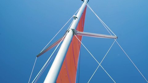 Lower angle view of a mast and mainsail with ropes of a sailing boat, isolated on a plain blue sky at summer,