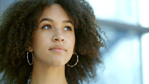 Beautiful young African American girl looks up and at camera. Portrait stylish woman, confident ethnic female student with curly hairstyle, freckles. Lady in urban city background. Real people series