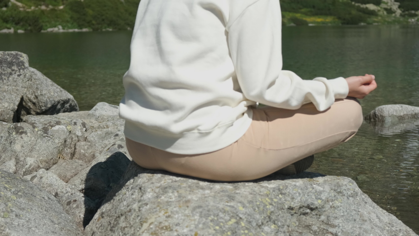 Young woman practising yoga on the lakeshore with amazing view on the waterfall and mountains. 