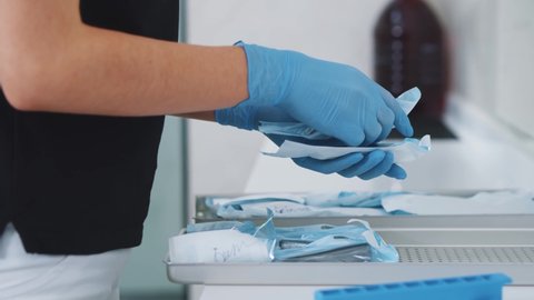 Female professional dentist preparing wrapped packages with dental instruments after autoclave sterilization process. Dental assistant. Stomatology.