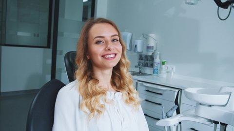 Dental health. Stomatology checkup. Beautiful young caucasian woman with perfect teeth smiling at camera on dentist's chair. Portraits. Hospital. Interiors.