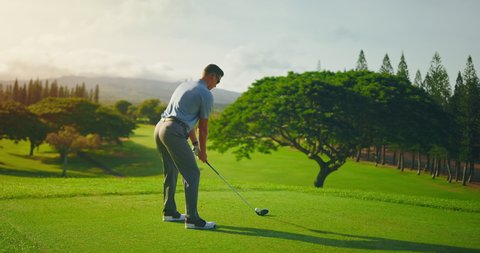 Man playing golf at sunrise, swinging and hitting golf ball, slow motion