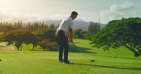 Man swinging and hitting golf ball on beautiful golf course at sunrise, slow motion