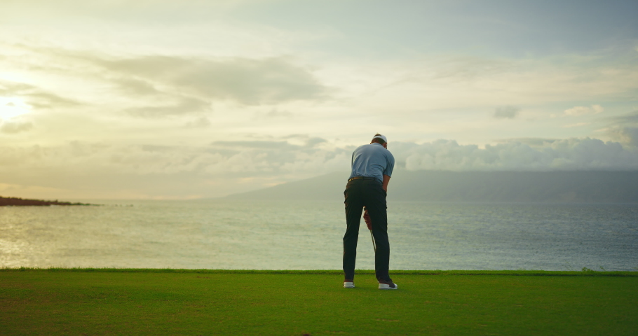 Sunset golf, man swinging and hitting golf ball on beautiful course by the ocean, slow motion