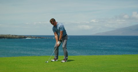Golfer swinging and hitting golf ball on beautiful course by the ocean, slow motion