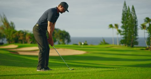 Man playing golf on beautiful luxury resort golf course, swinging and hitting golf ball in slow motion